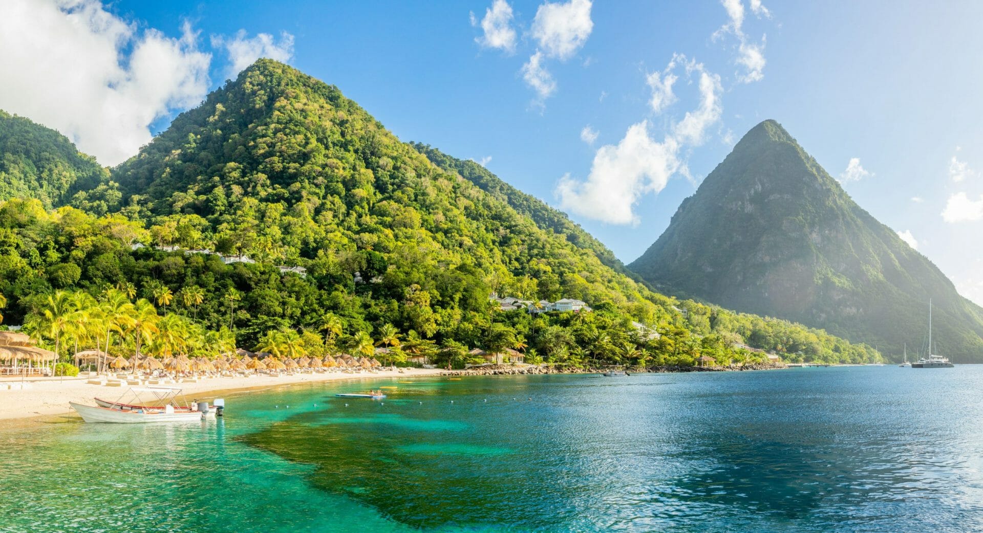 Playa caribeña con palmeras y sombrillas de paja en la orilla, con el monte Gros Piton en el fondo. Sugar Beach, Santa Lucía