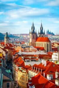 Altas agujas de las torres de la Iglesia de Týn en la ciudad de Praga (Catedral de Nuestra Señora antes de Týn), paisaje urbano panorámico con tejados rojos de casas en la Ciudad Vieja y cielo azul con nubes